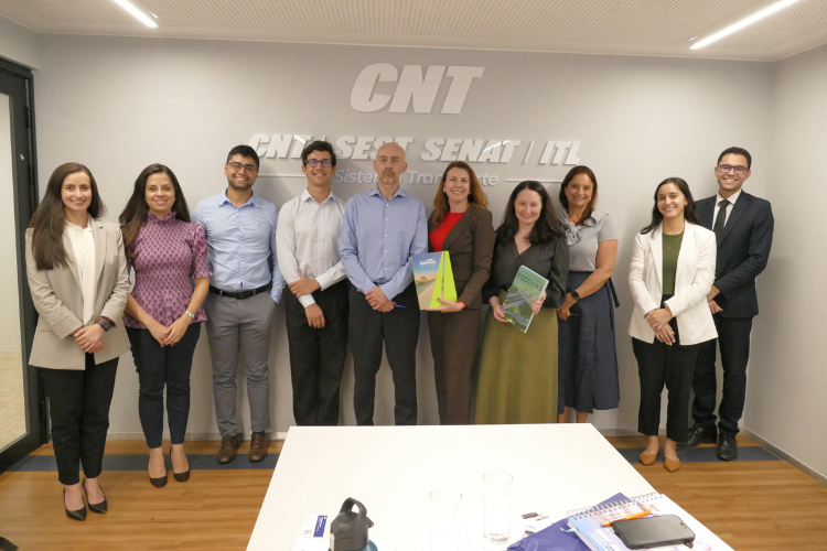 Grupo de oito pessoas posa de frente para a foto tendo ao fundo parede cinza com os dizeres CNT